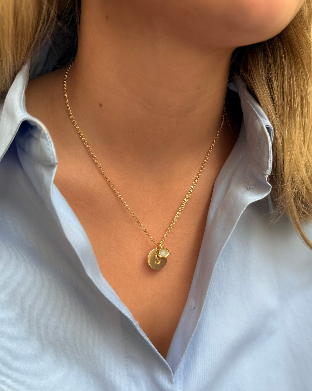 A necklace with two pendants: a March birthstone featuring a light blue aquamarine and a gold letter S pendant.
