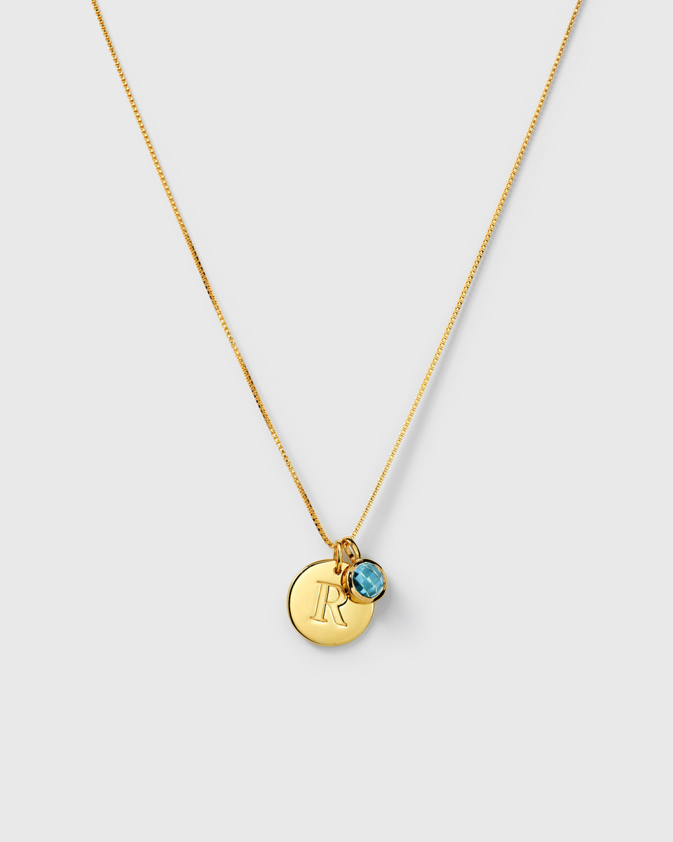 Gold necklace featuring a September birthstone blue topaz pendant and a round letter charm on the same chain.