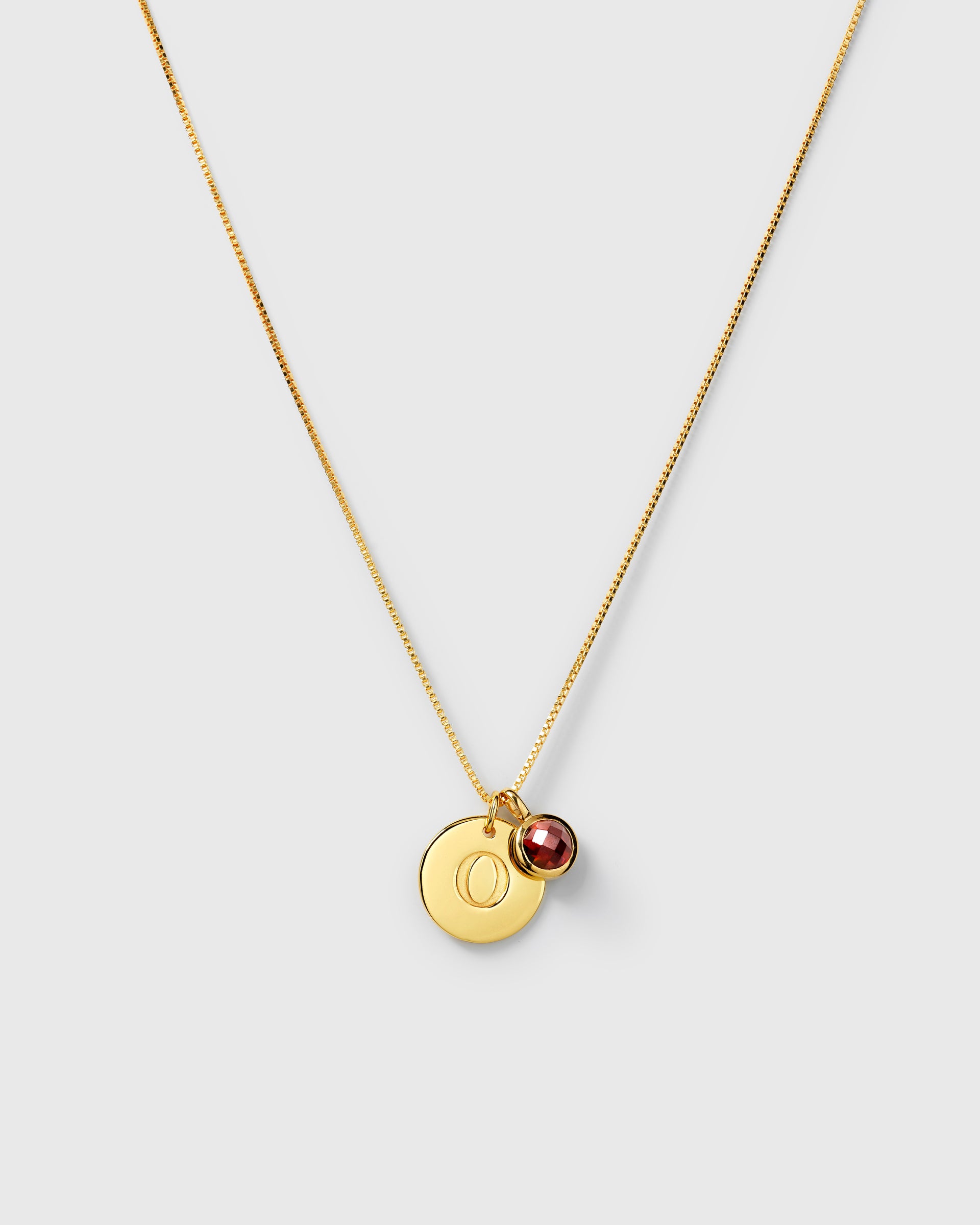 Gold necklace with two pendants: a January birthstone red garnet and a round letter charm.