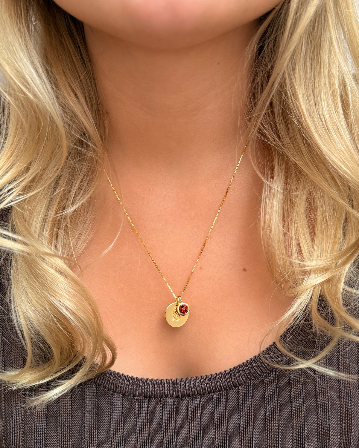 A necklace with two pendants: a January birthstone featuring a garnet, styled with a gold mini letter pendant on a delicate gold chain.