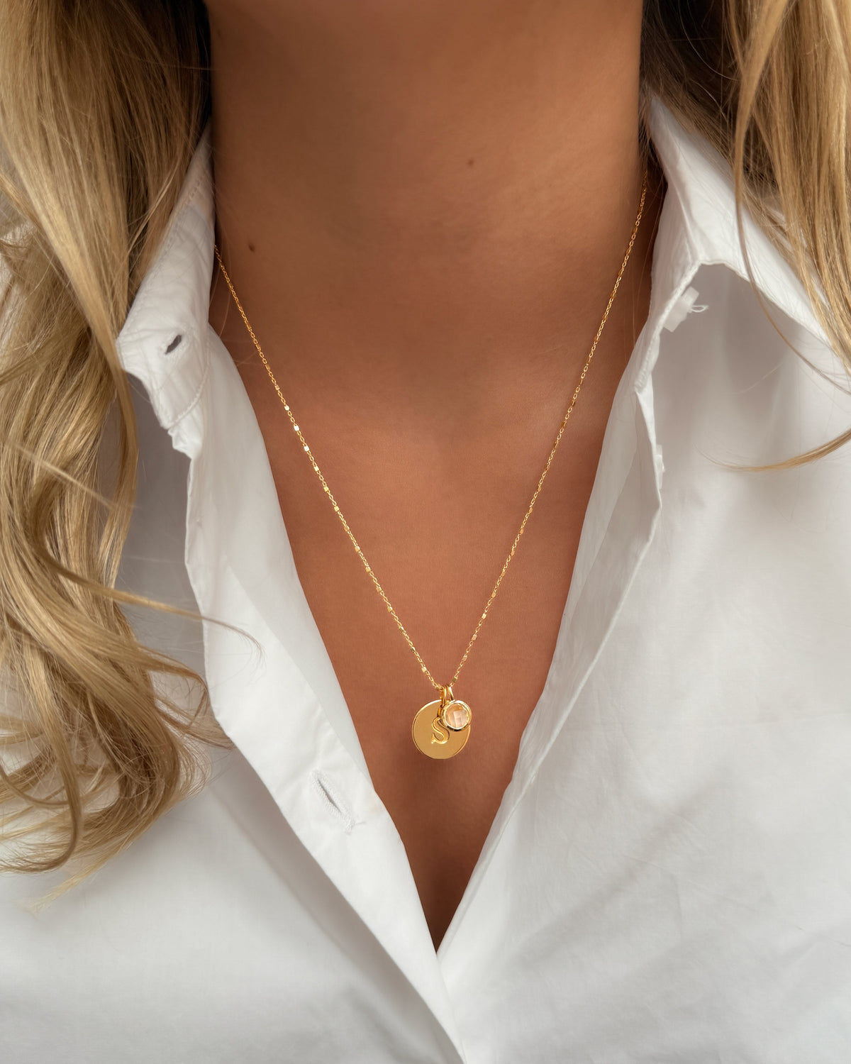 A gold pendant necklace featuring the June birthstone moonstone, layered with a delicate gold chain and a round letter pendant.