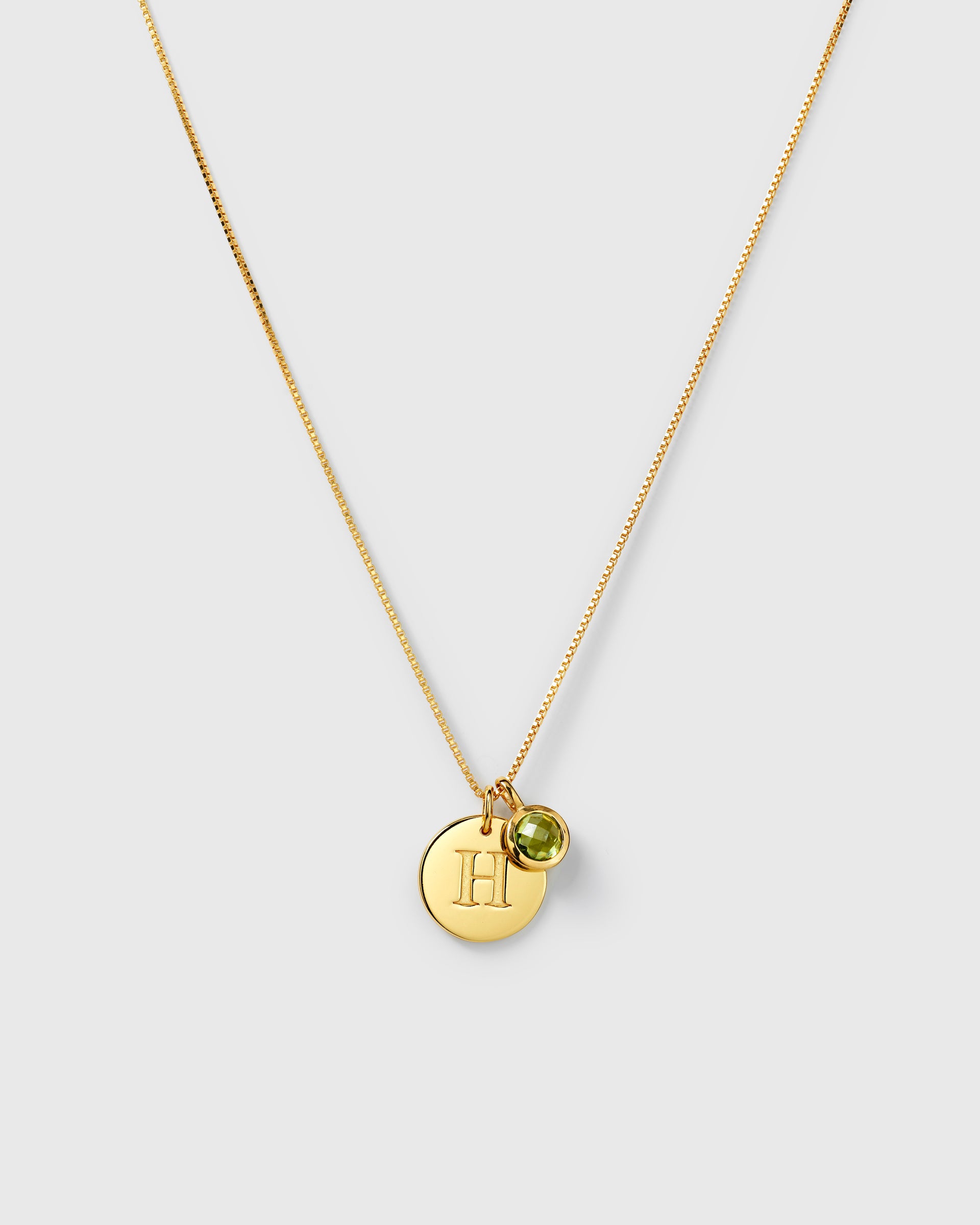 Gold necklace with two pendants: an August birthstone green peridot and a round letter charm.