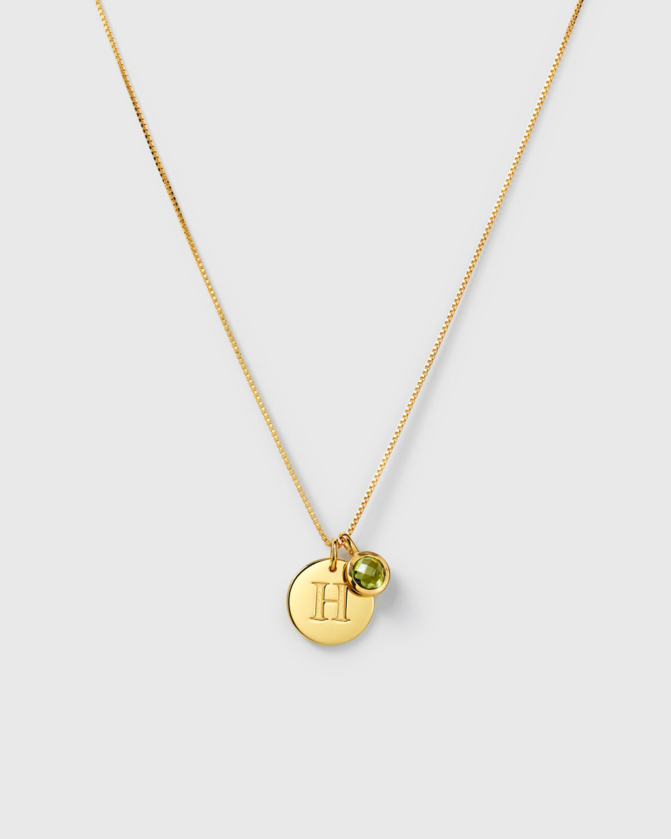 Gold necklace with two pendants: an August birthstone green peridot and a round letter charm.