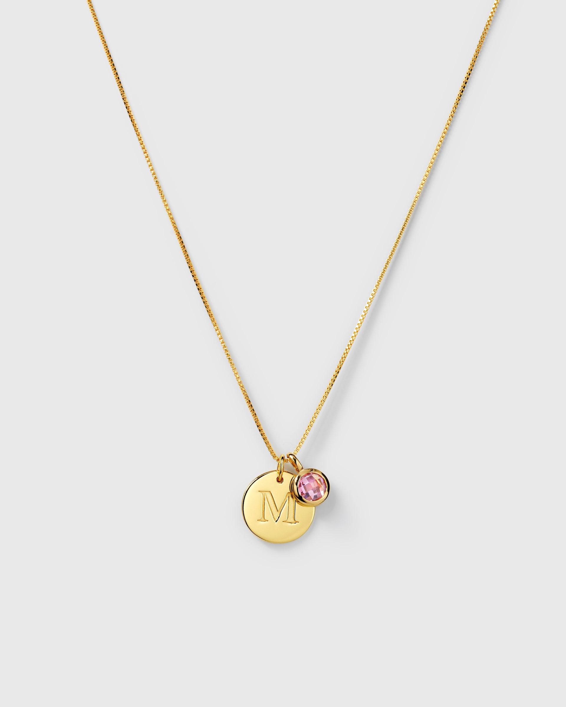 Gold necklace with two pendants: an October birthstone pink tourmaline and a round letter charm.