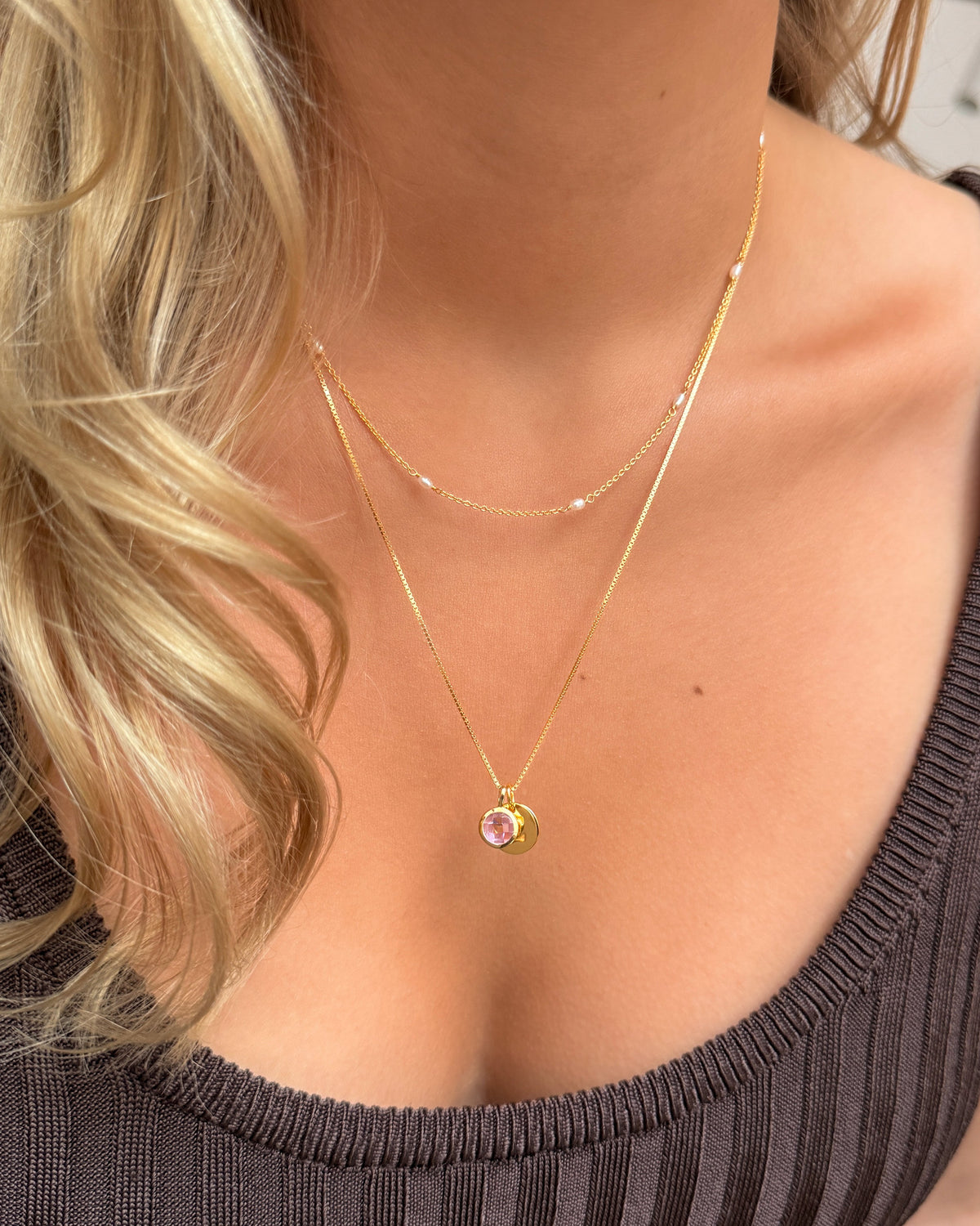 Two layered gold necklaces: a longer pendant necklace featuring the October birthstone pink tourmaline, paired with a shorter delicate pearl chain.