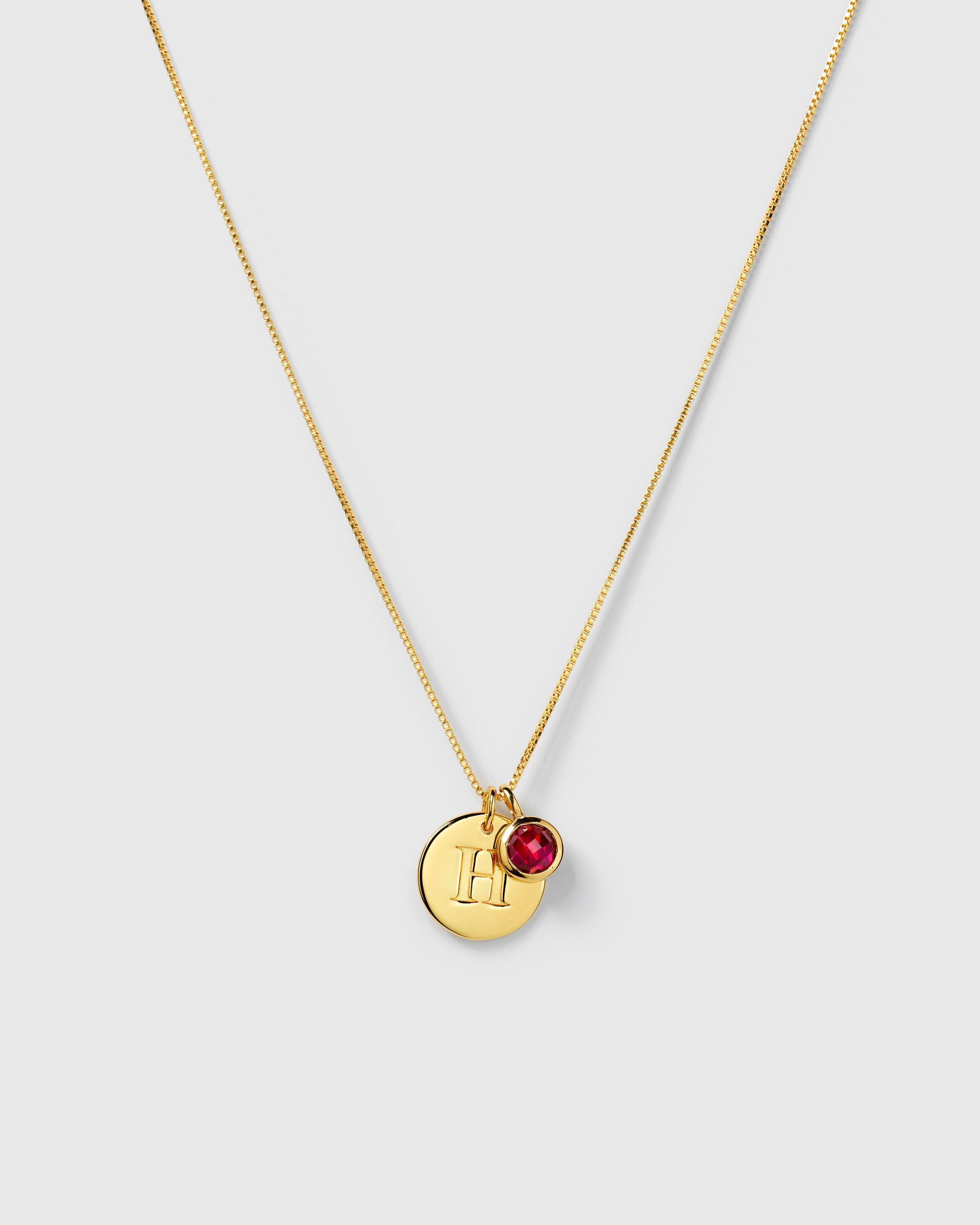 Gold necklace with two pendants: a July birthstone ruby and a round letter charm.