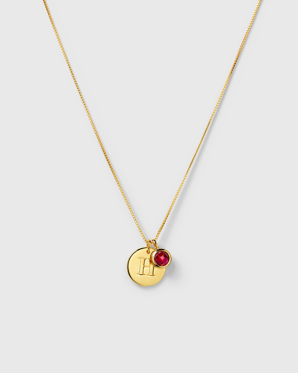 Gold necklace with two pendants: a July birthstone ruby and a round letter charm.