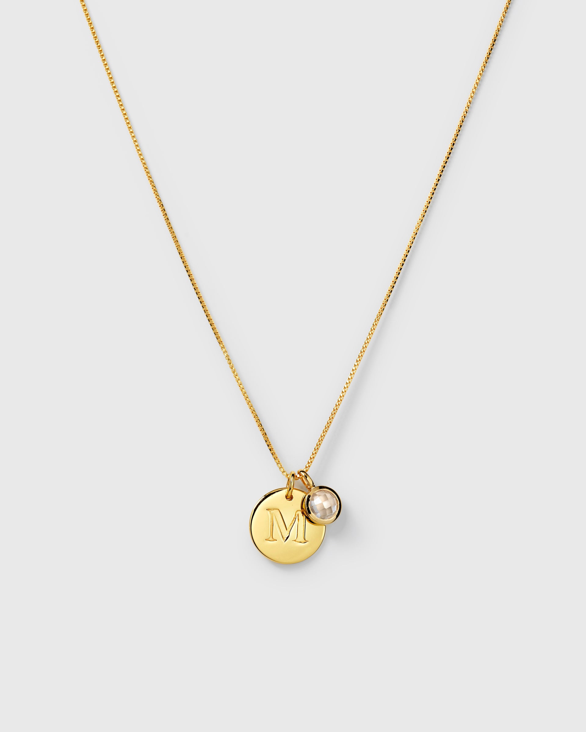 Gold necklace with two pendants: an April birthstone white topaz and a round letter charm.
