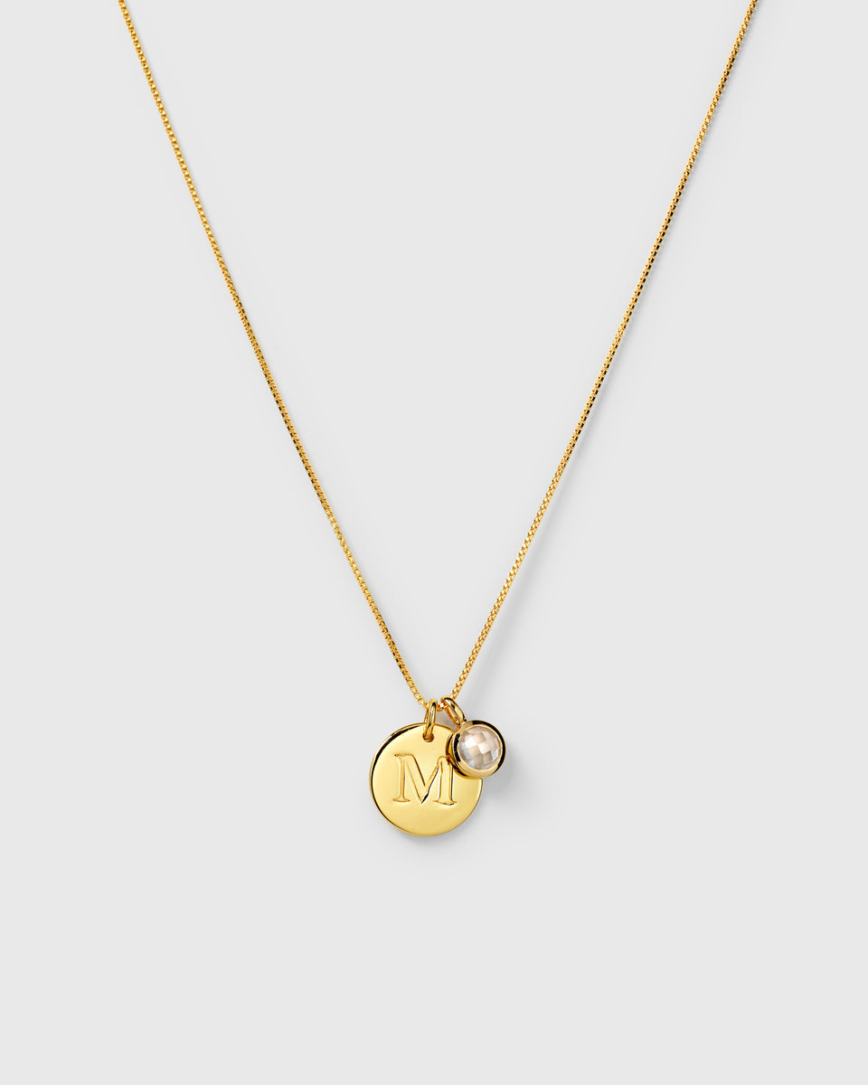 Gold necklace with two pendants: an April birthstone white topaz and a round letter charm.