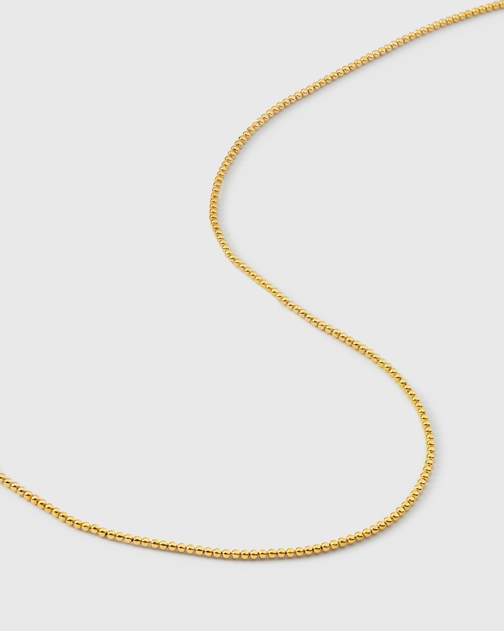 A product shot of the Syster P Sheer Doria Necklace in gold, featuring a delicate chain design composed of small, round beads.