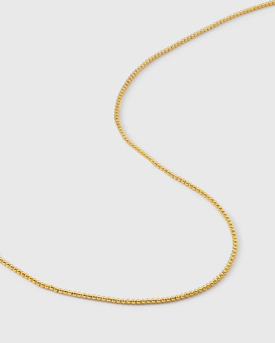 A product shot of the Syster P Sheer Doria Necklace in gold, featuring a delicate chain design composed of small, round beads.