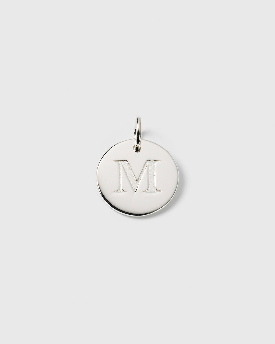 A product shot of the Syster P Beloved Big Letter Silver charm, featuring a round pendant with the letter 'M' engraved on the front.