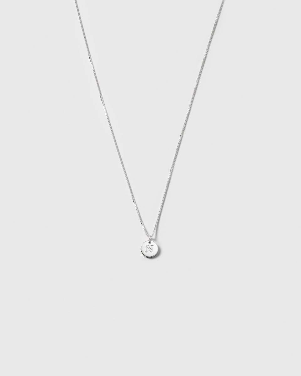 A product shot of the Beloved Medium Box Chain in silver, styled with a small, circular pendant engraved with the letter N.