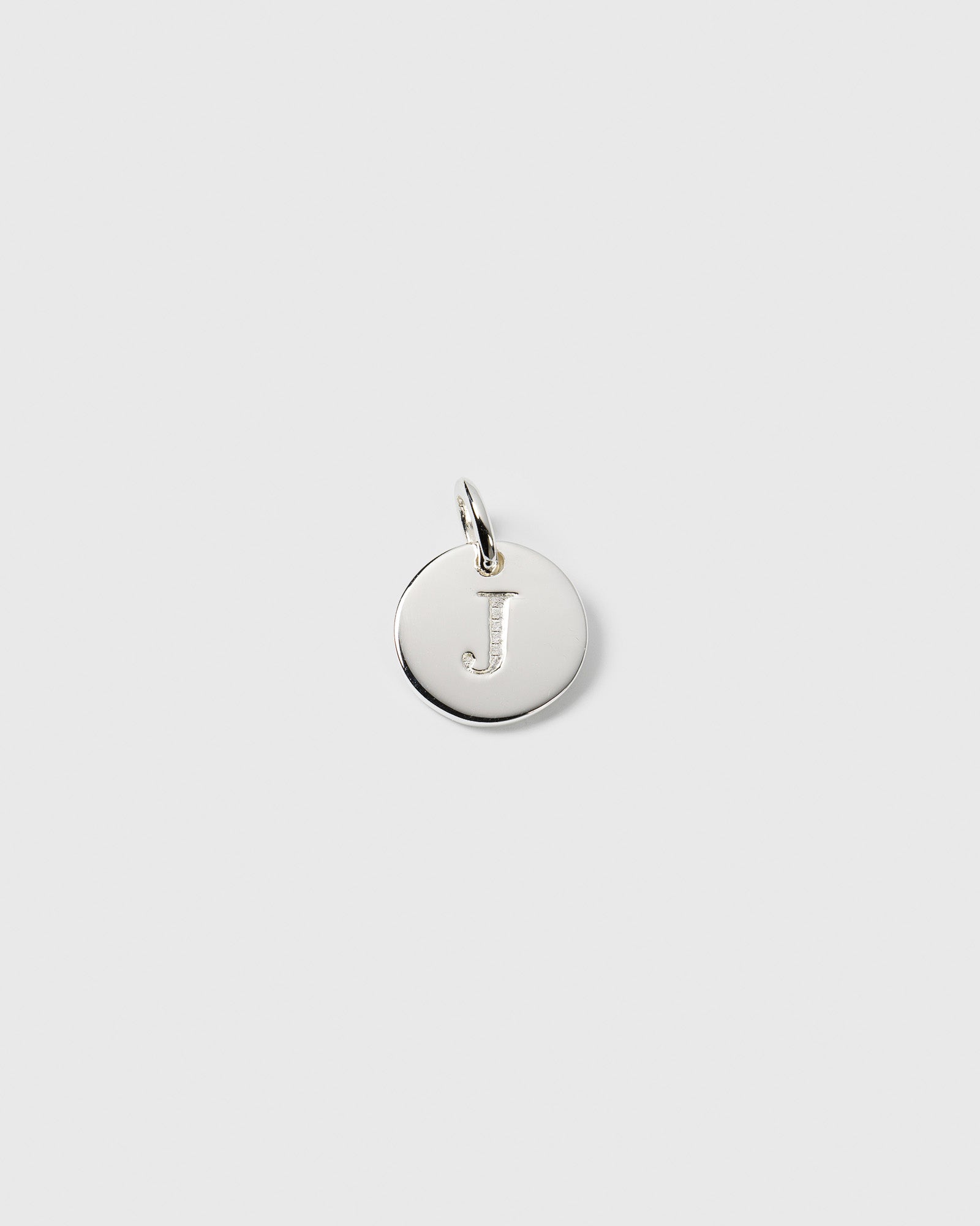 A product shot of the Beloved Mini Letter 'J' pendant in silver, a small circular charm with the initial engraved on the front.