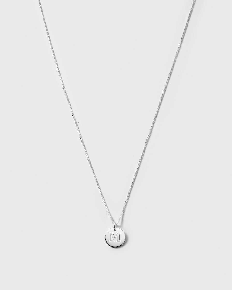 A product shot of the Beloved Long Box Chain in silver, shown with a round silver pendant engraved with the letter 'M'.