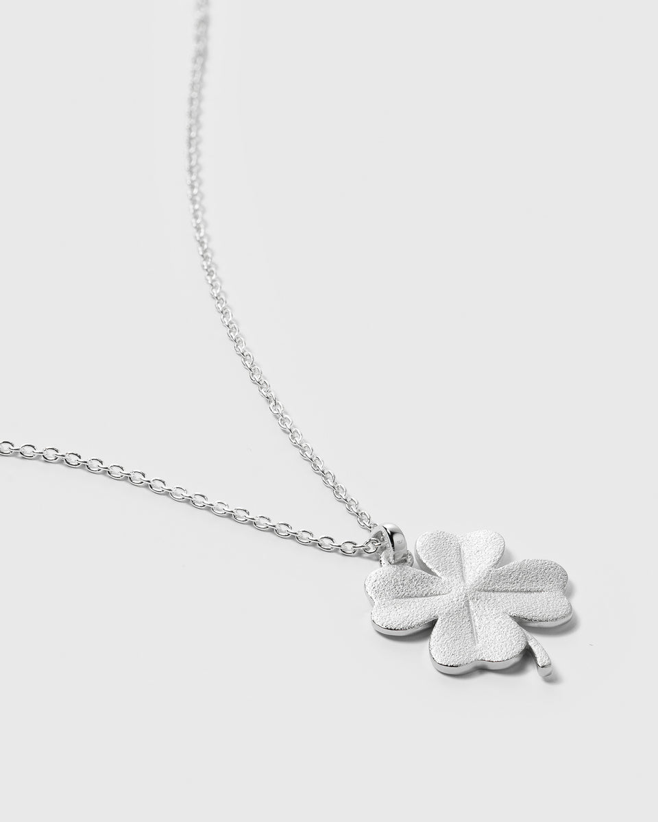 A close-up product shot of the Beaches Fortune Necklace in silver, showcasing its matte four-leaf clover pendant and delicate oval link chain.