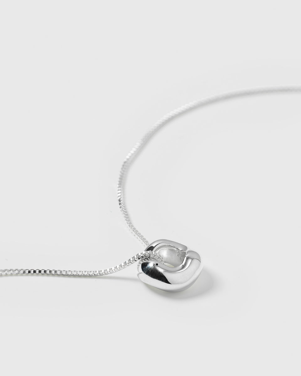 A close-up product shot of the Bolded Wavy Necklace in silver, highlighting its shiny and smooth wavy pendant on a delicate chain.