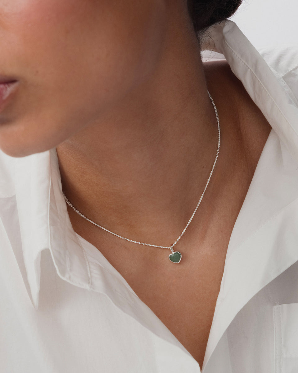A model wearing a delicate silver chain necklace with a small, heart-shaped green jade pendant.