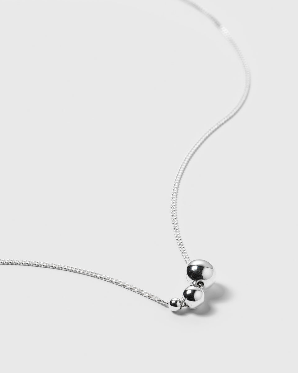 A product shot of the Universe Necklace in silver, featuring a delicate chain adorned with a cluster of three polished silver balls in varying sizes.
