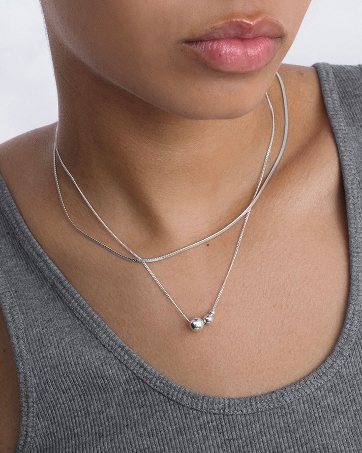 A close-up shot of a model wearing the Universe Necklace Silver, featuring three small silver balls on a fine chain, layered with a simple silver snake chain.