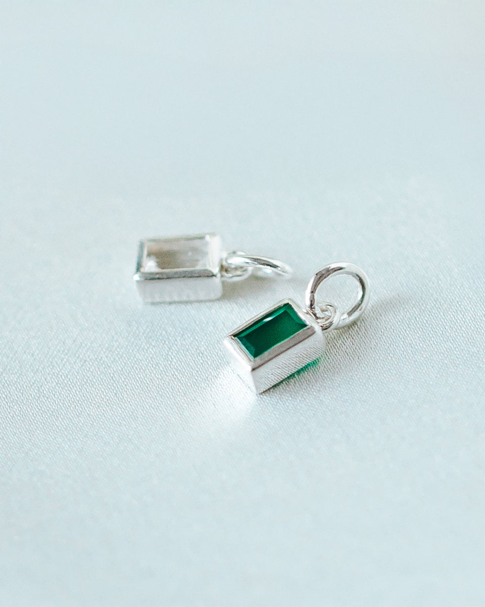 A product shot of two Beloved Squared Pendants in silver, one featuring a green onyx stone in the foreground and the other a clear crystal in the background.