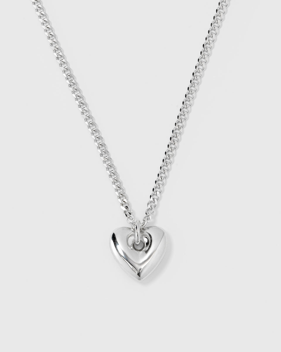 A product shot of the Fat Heart Necklace in silver, featuring a chunky curb chain and a large, puffy heart-shaped pendant.