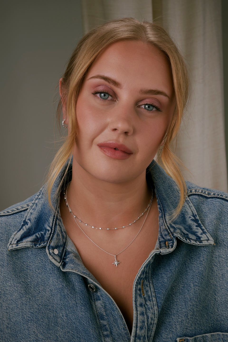 A shot of a model wearing the North Star Big Necklace in silver, featuring a star-shaped pendant with a crystal, layered with a shorter, twisted herringbone-style silver necklace.