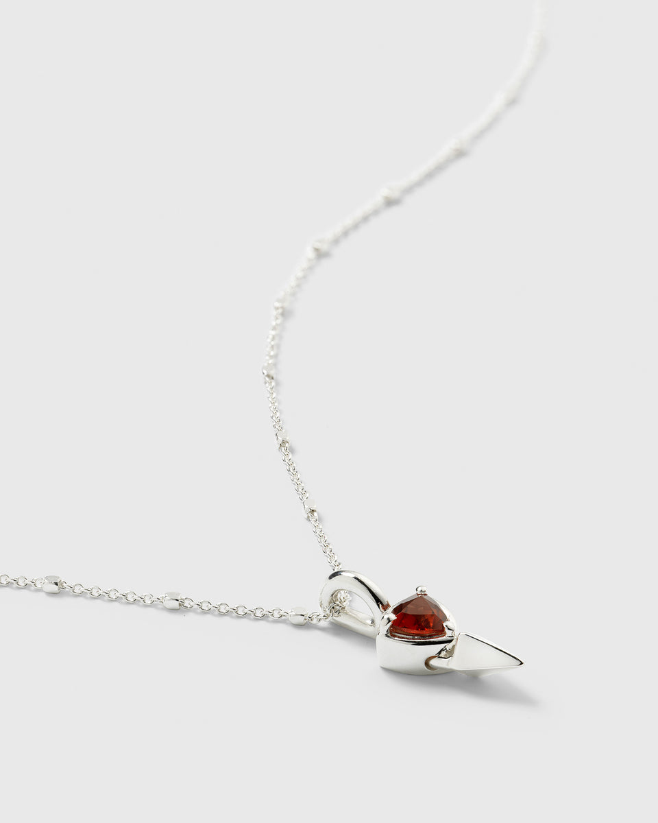 A close-up shot of the Mrs H Spike Necklace in silver, showcasing its pendant which features a sharp spike alongside a deep red garnet stone on a delicate beaded chain.