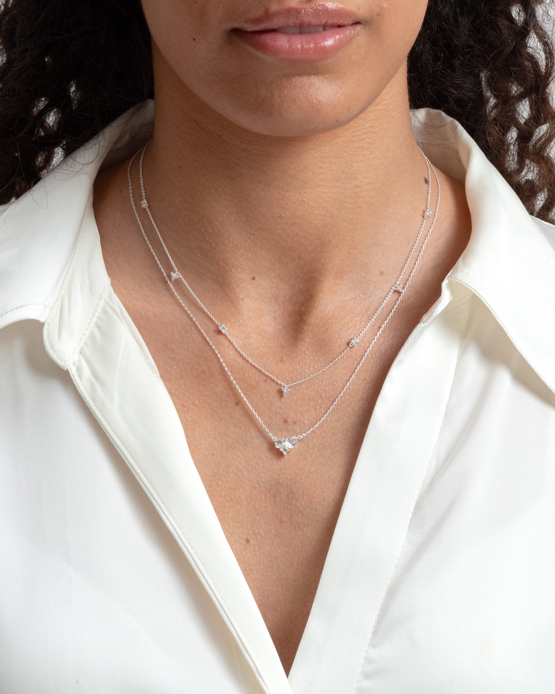 A close-up shot of a model wearing the silver Celestia Necklace, featuring a delicate chain with a central cluster of cubic zirconias, layered with a similar fine chain necklace.