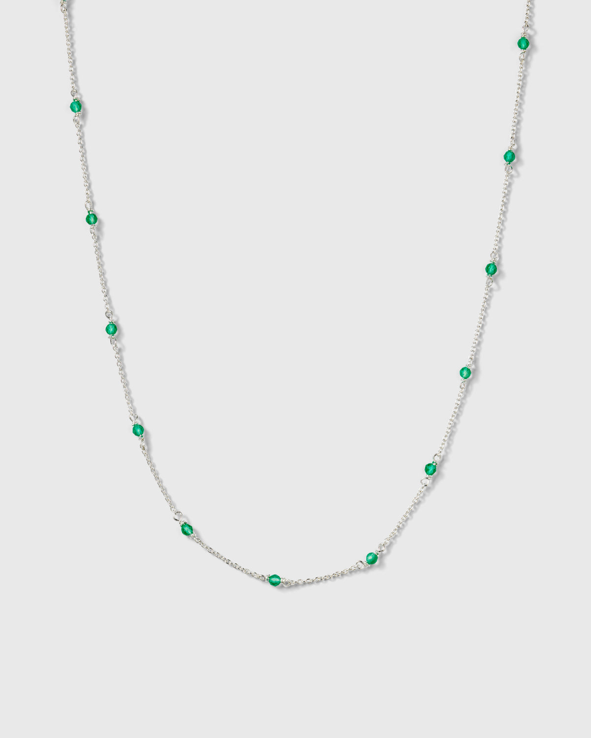 A product shot of the Santa Monica Necklace in silver, featuring a delicate chain with small, vibrant green onyx stones spaced throughout.