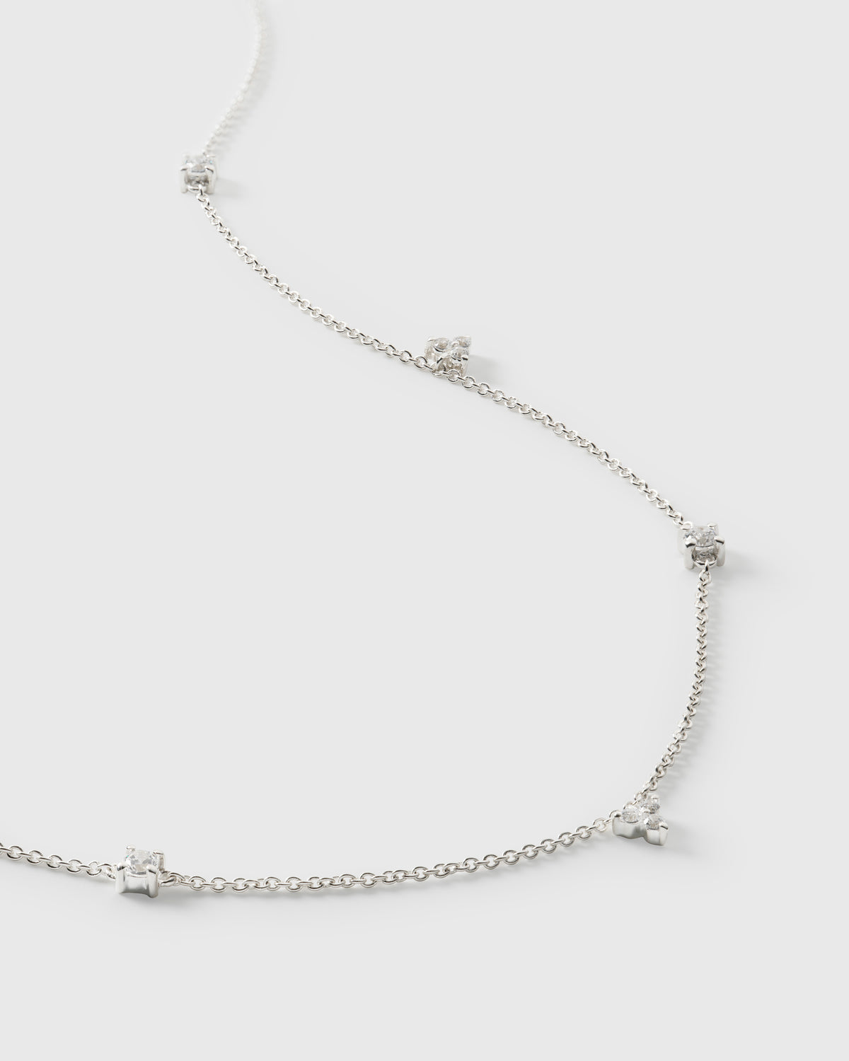 A product shot of the Celestia Necklace in silver, laid out to showcase its delicate chain which is adorned with sparkling cubic zirconia stones in various shapes.