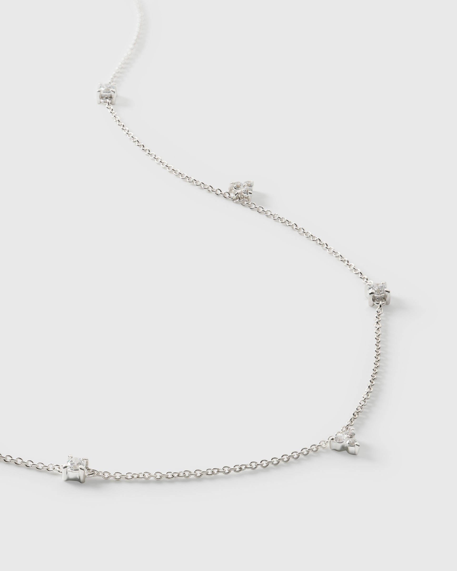 A product shot of the Celestia Necklace in silver, laid out to showcase its delicate chain which is adorned with sparkling cubic zirconia stones in various shapes.