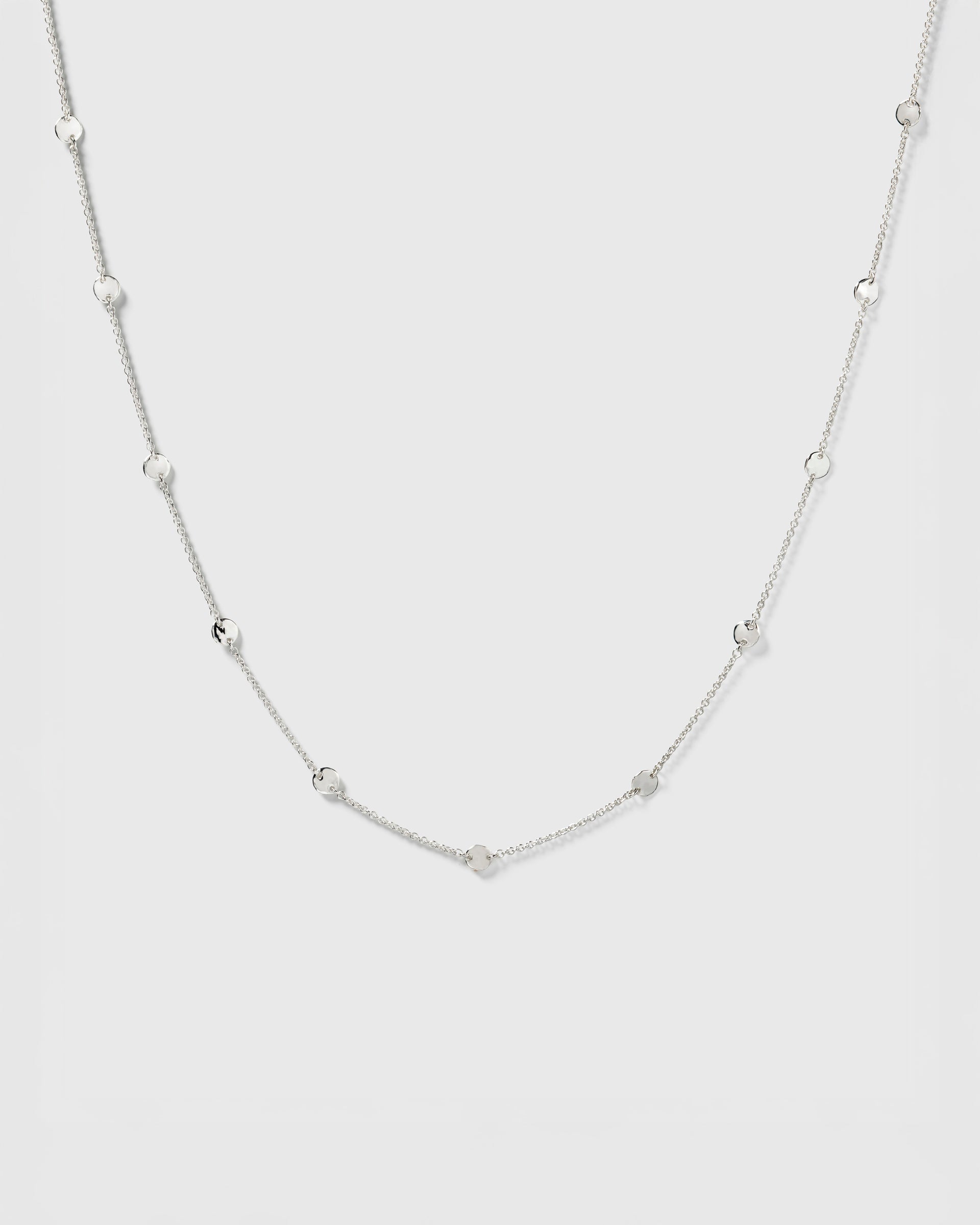 A product shot of the Solea Necklace in silver, laid out to showcase its design of a fine chain adorned with small, round, hammered circles.