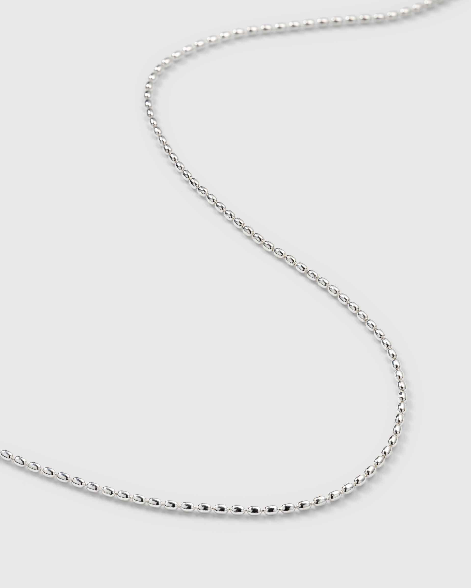 A close-up product shot of the Lunetta Necklace in silver, laid out in a curve to display the detail of its chain made from small oval beads.