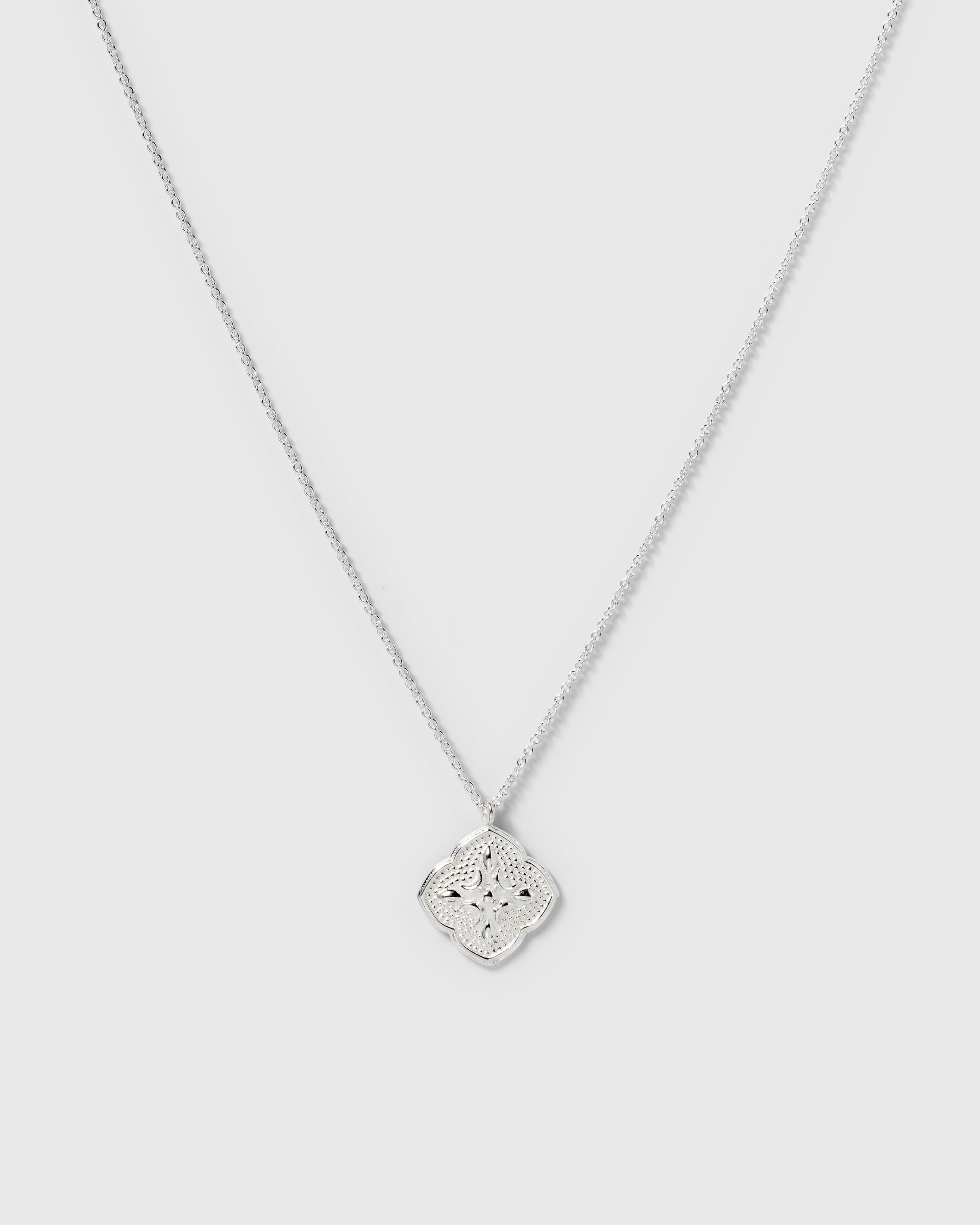A product shot of the Luna Necklace in silver, featuring a delicate chain and a large, intricately patterned pendant inspired by the moon.