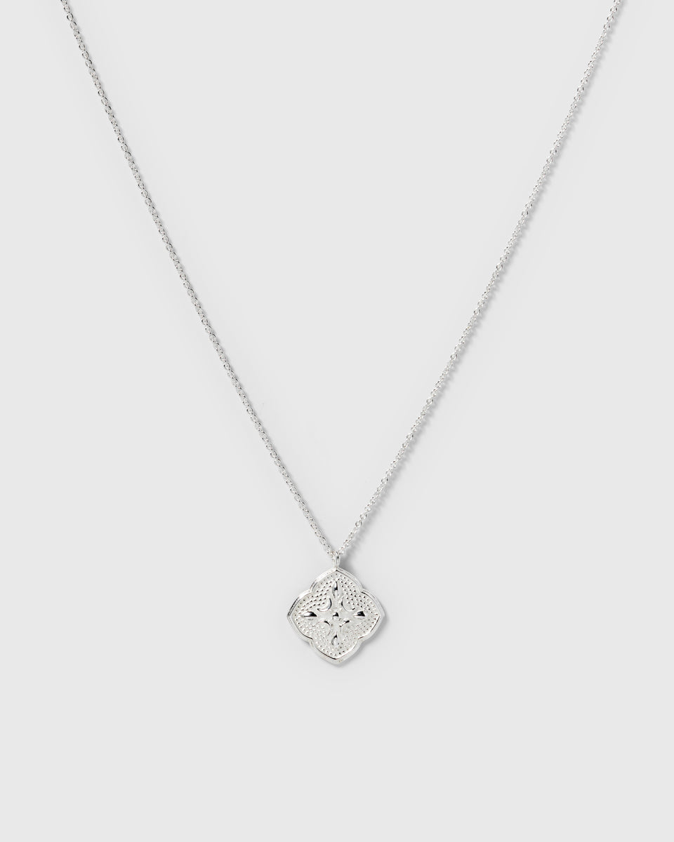 A product shot of the Luna Necklace in silver, featuring a delicate chain and a large, intricately patterned pendant inspired by the moon.