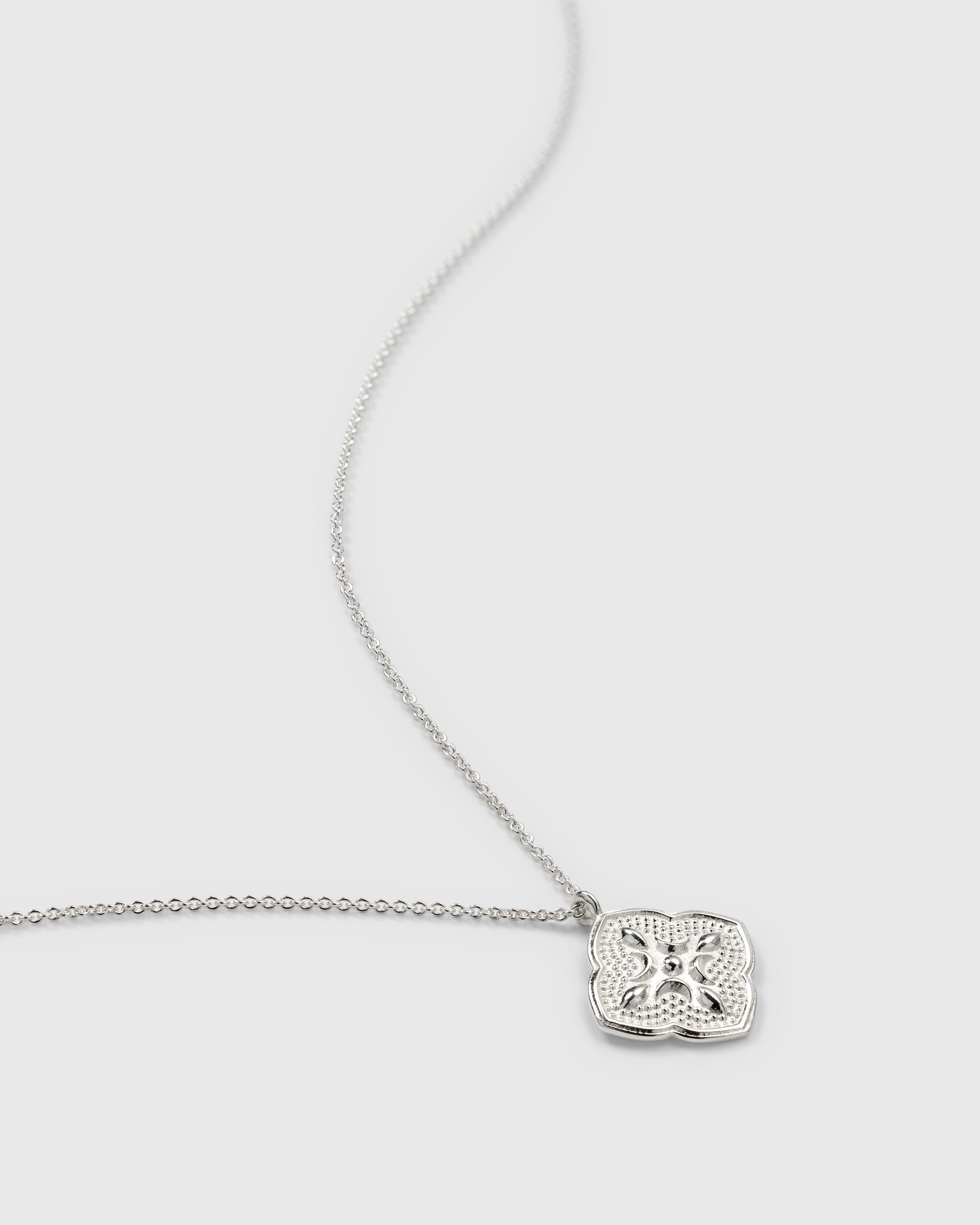 A close-up shot of the Luna Necklace in silver, showcasing its quatrefoil-shaped pendant with an intricate, moon-inspired design.