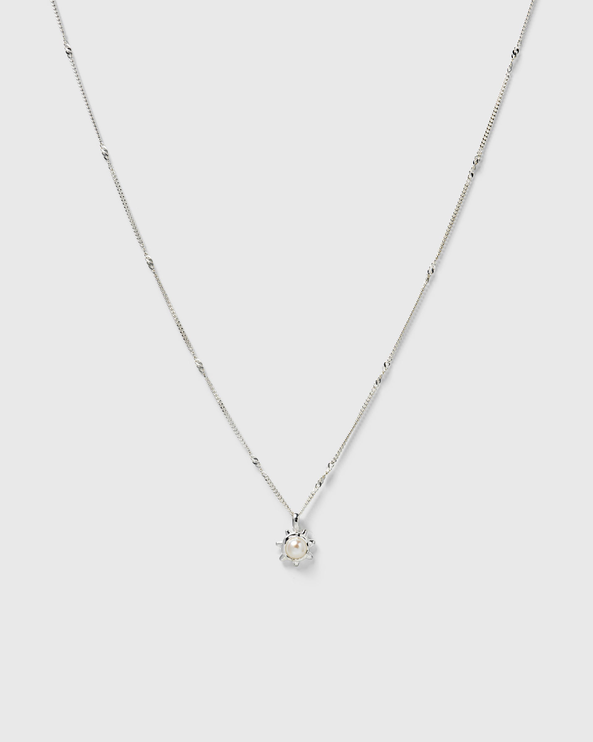 A silver necklace with a delicate chain and a sunburst pendant featuring a freshwater pearl.