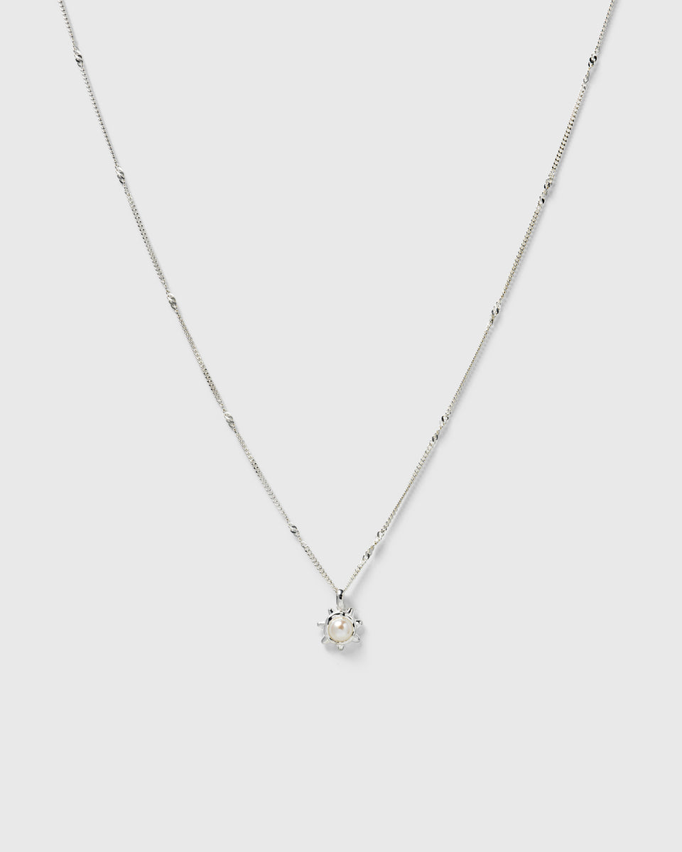 A silver necklace with a delicate chain and a sunburst pendant featuring a freshwater pearl.