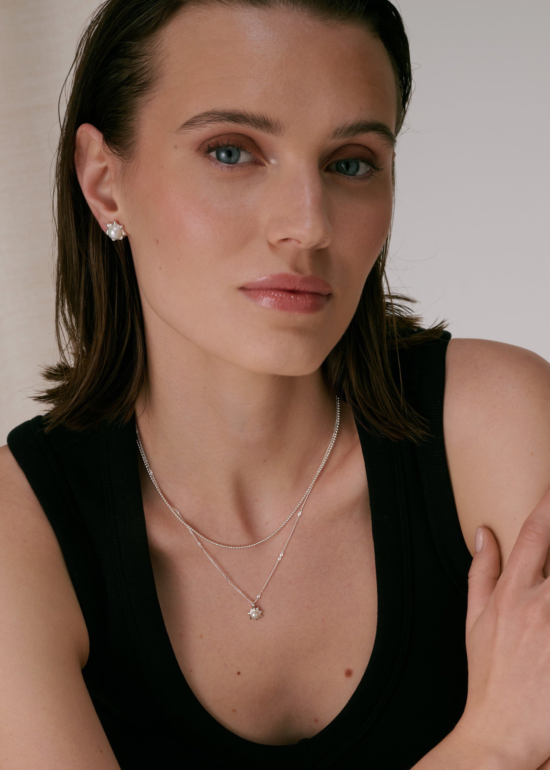 A silver necklace with a flower-shaped pendant featuring a freshwater pearl, layered with another silver chain, paired with matching pearl stud earrings.