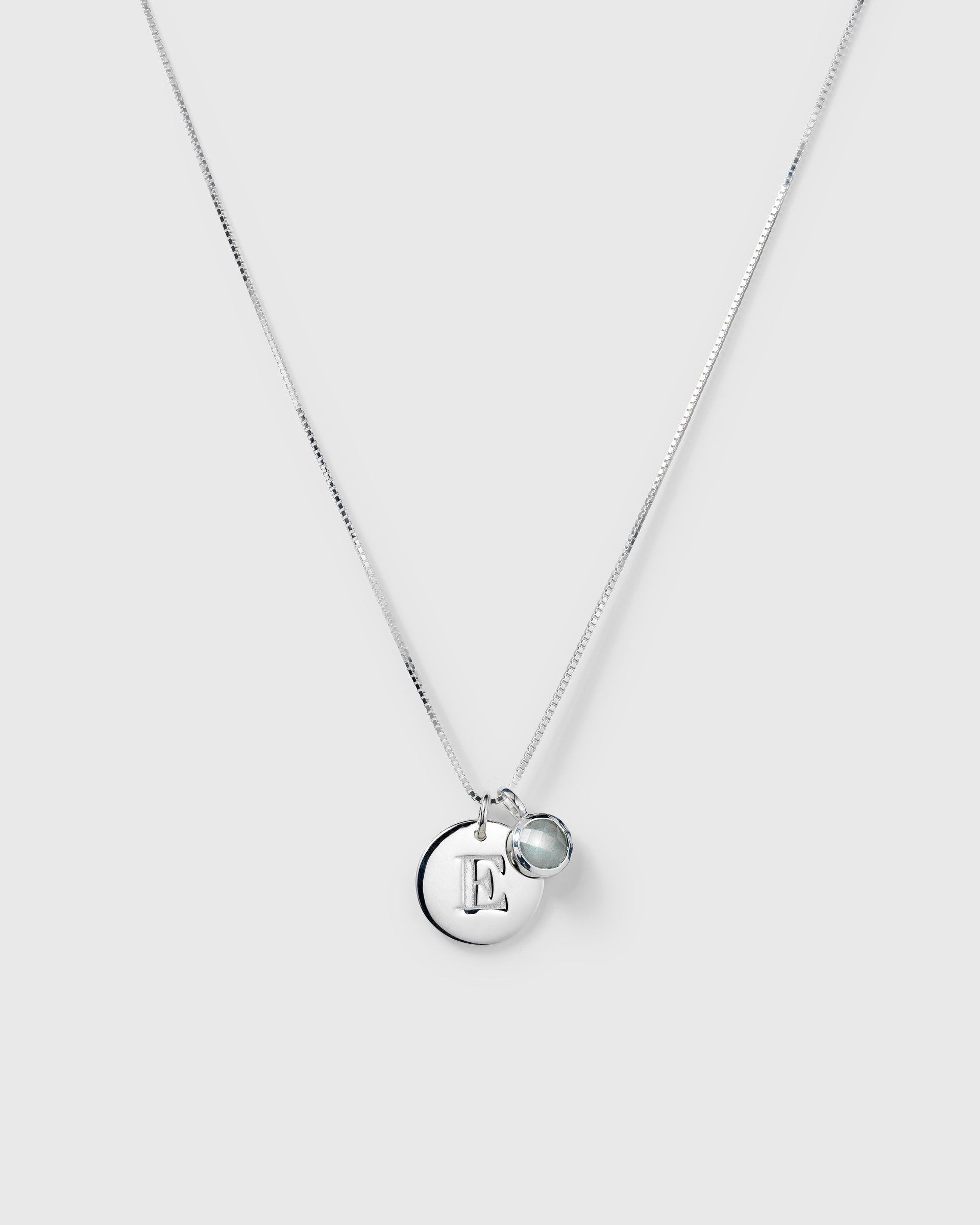Silver necklace with two pendants: a March birthstone aquamarine and a round letter charm.