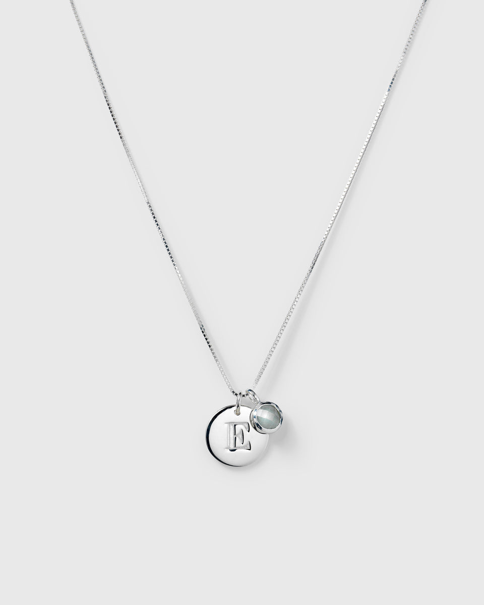 Silver necklace with two pendants: a March birthstone aquamarine and a round letter charm.