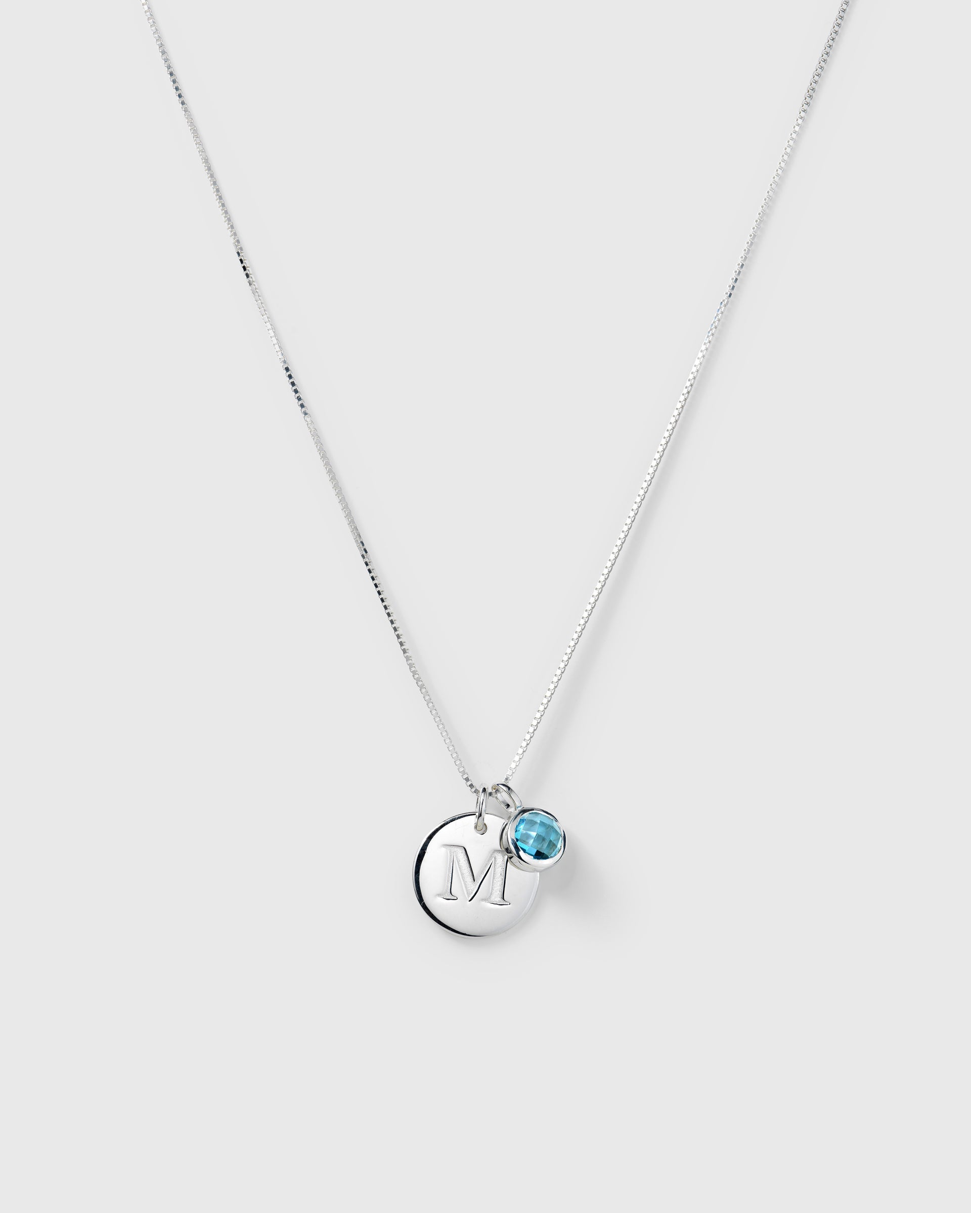 Silver necklace with two pendants: a September birthstone blue topaz and a round letter charm.
