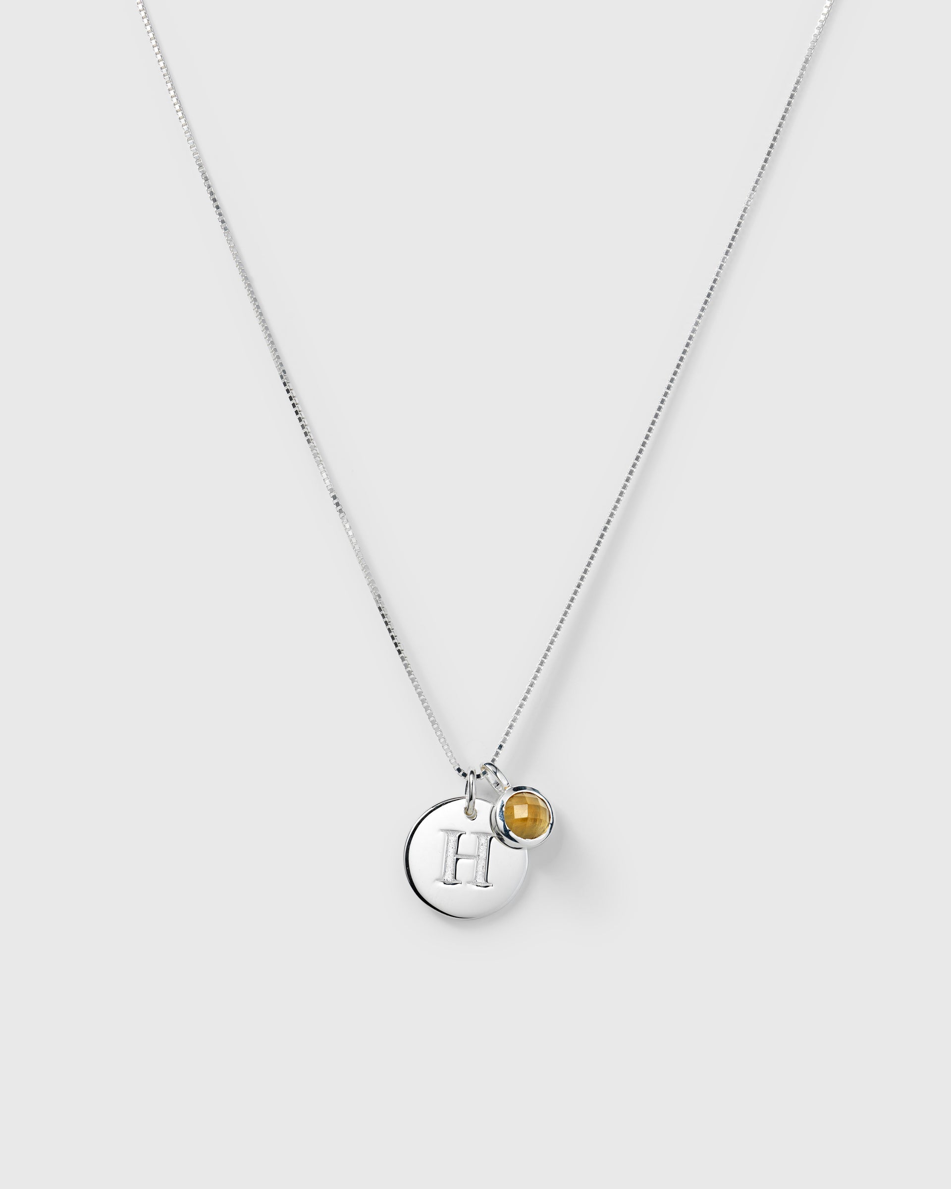 Silver necklace with two pendants: a November birthstone yellow citrine and a round letter charm.