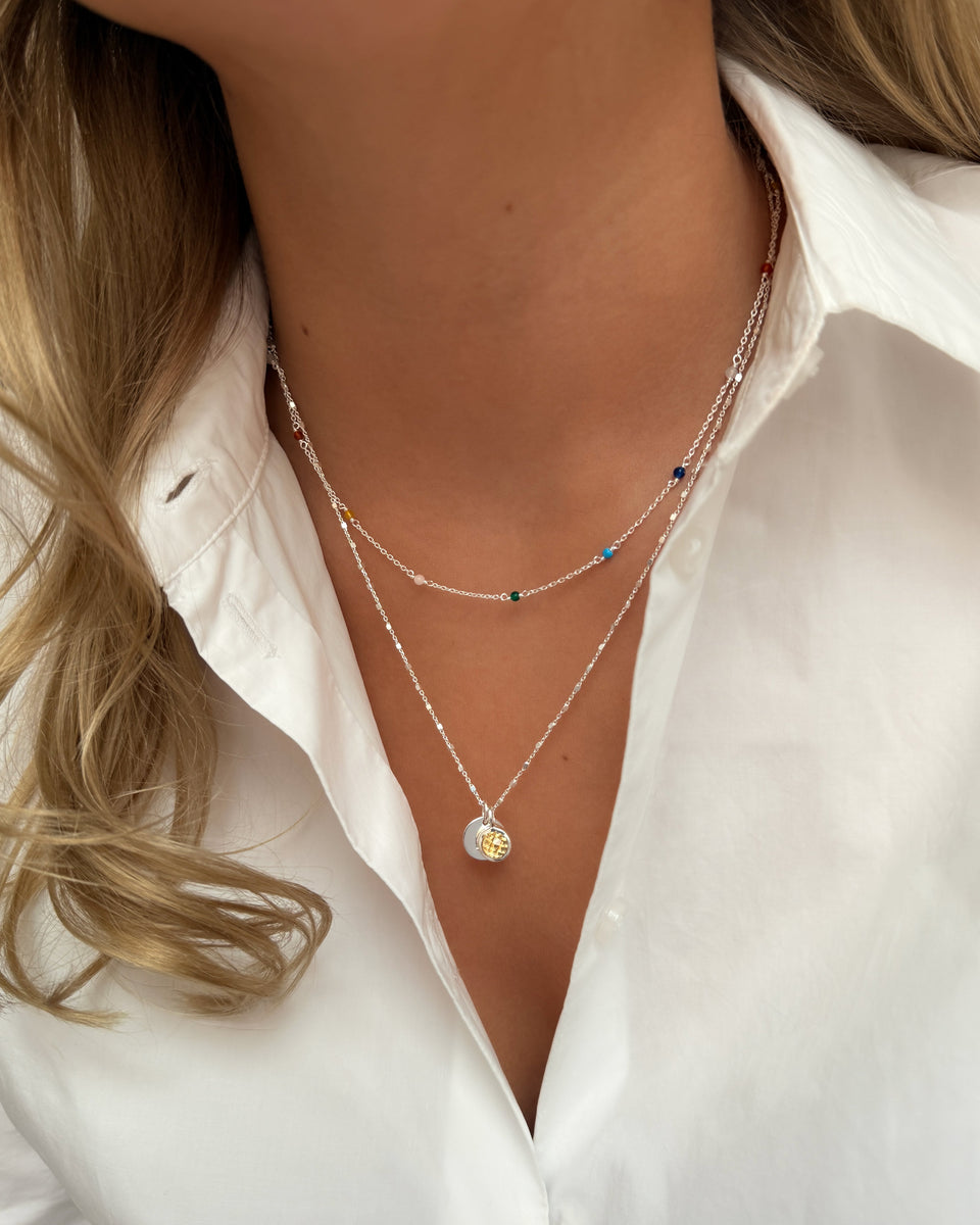 Two silver necklaces layered: November birthstone citrine pendant and a chain with small colorful beads.
