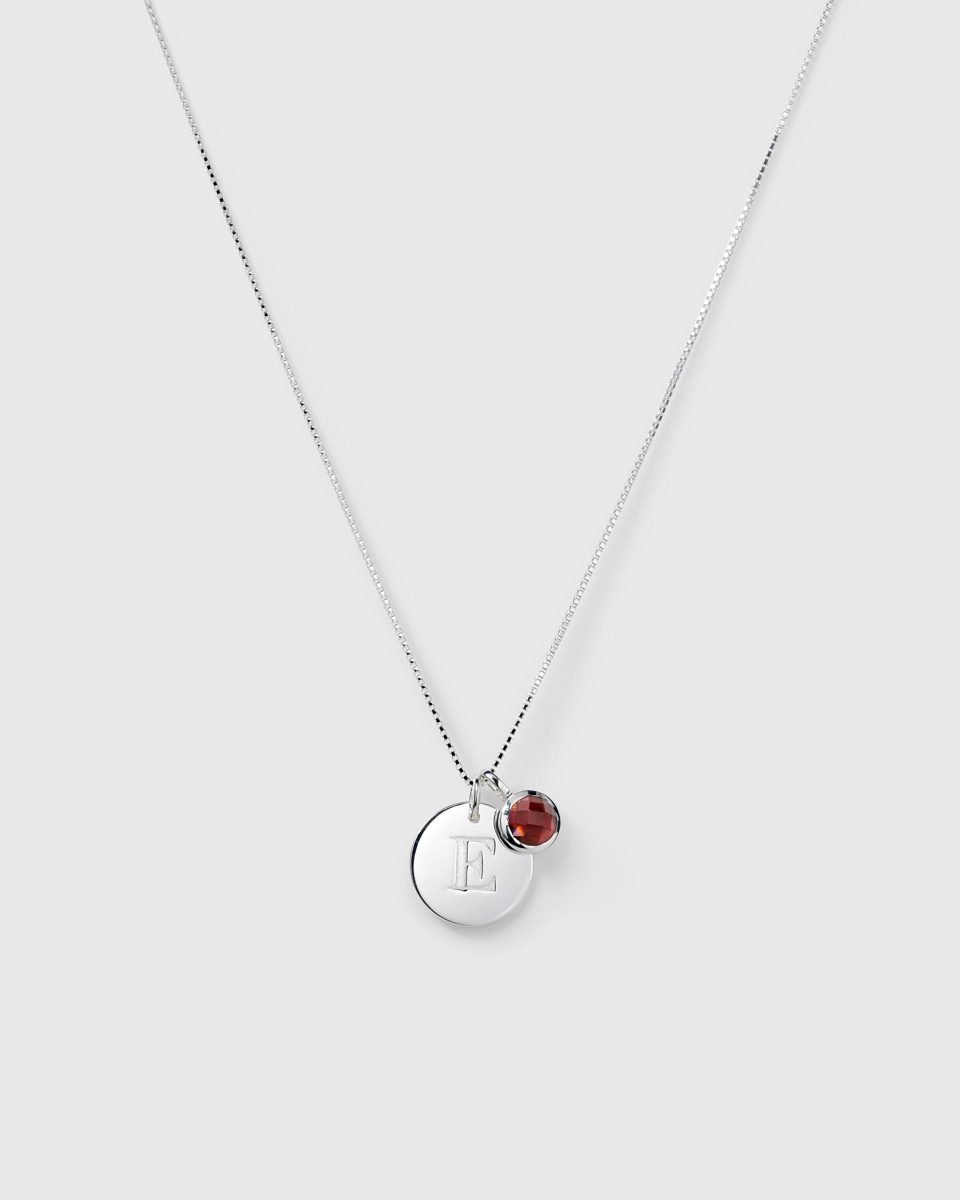 Silver necklace with two pendants: a January birthstone red garnet and a round letter charm.