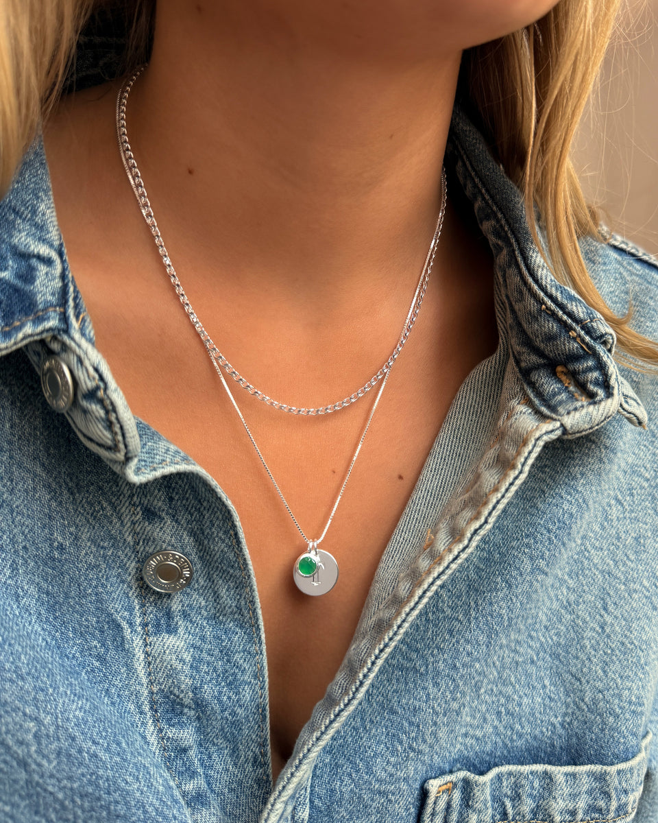 Two layered silver necklaces: a curb chain and a delicate chain with a May birthstone pendant featuring a round green onyx stone.