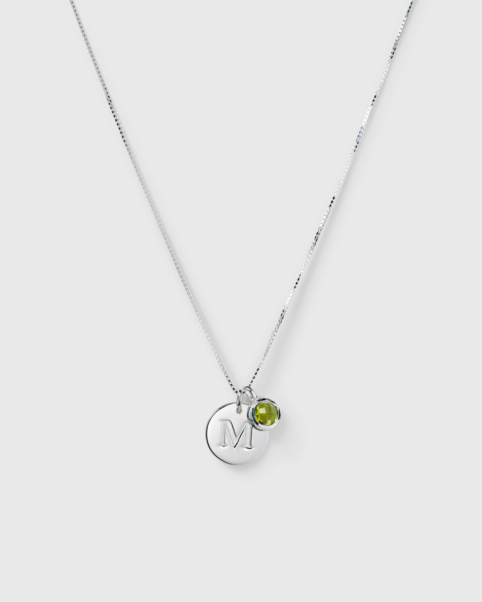 Silver necklace with two pendants: an August birthstone green peridot and a round letter charm.