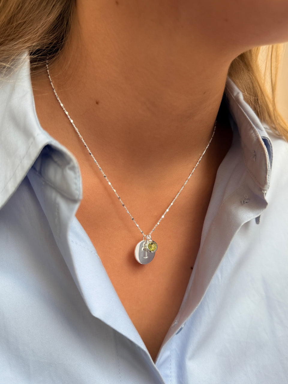 A necklace featuring an August birthstone pendant with a green peridot, accented by a round silver letter charm.