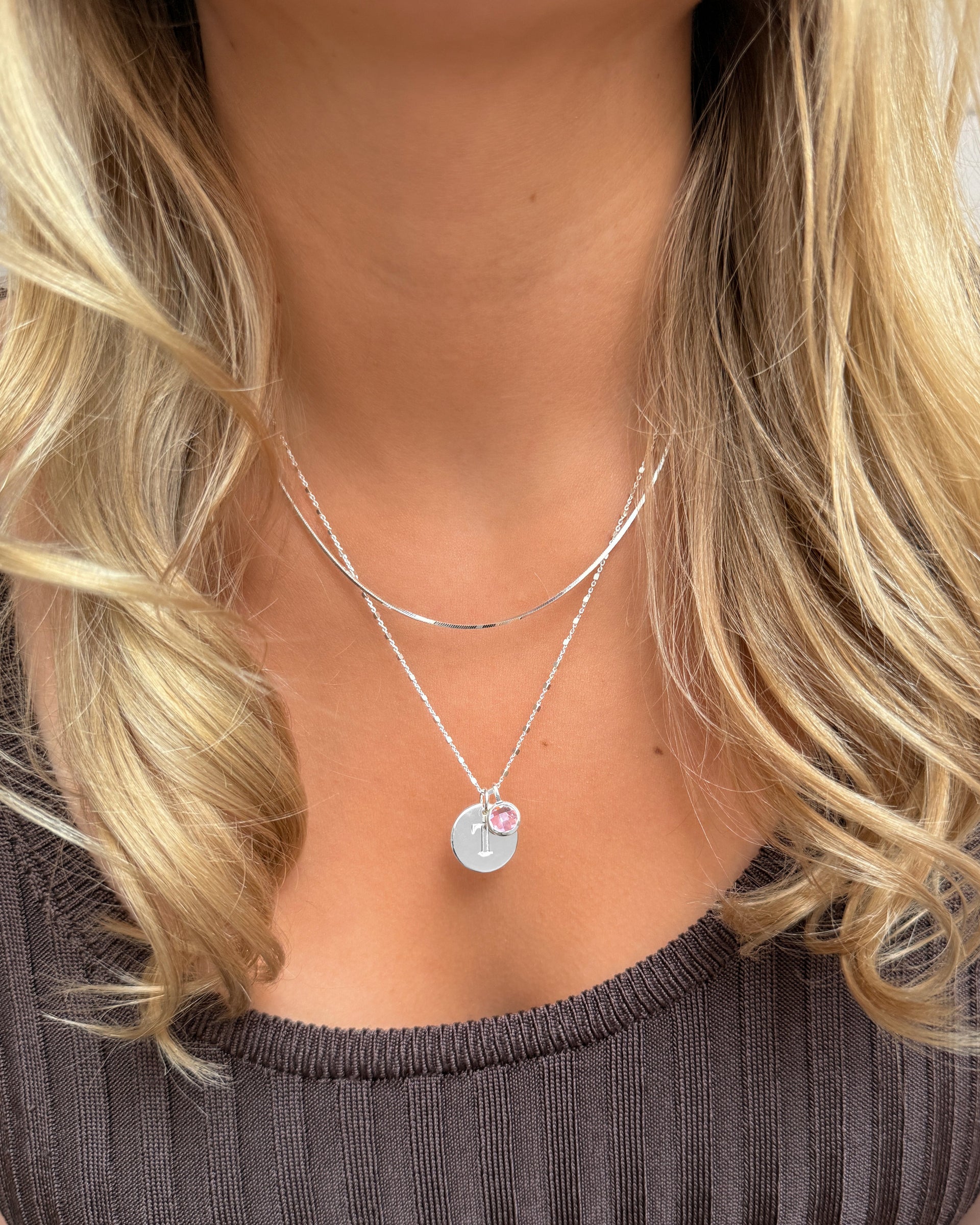 Layered silver necklaces with letter charm and October birthstone pink pendant.